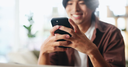 Texting, happy or Asian man in home with phone, online chat or communication on dating site. Smile, flare or male person in house with tech, digital app or connection on matchmaking platform.の写真素材