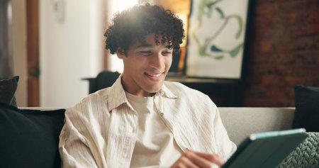 Tablet, smile and man in home, typing for communication and message to contact. Online humor, tech and person on sofa, subscription and digital app for social media, entertainment and website infoの写真素材
