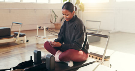 Woman, phone and chat at pilates studio with smile for exercise update, social media break and texting. Female person relax on reformer, fitness and mobile app for health progress or blog at club
