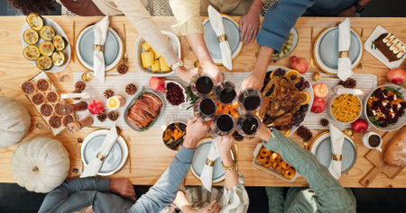 Thanksgiving, wine and cheers with hands of family for festive feast, celebration and dinner. Toast, alcohol drink and holiday season with above of people and glass in dining room of home for reunion