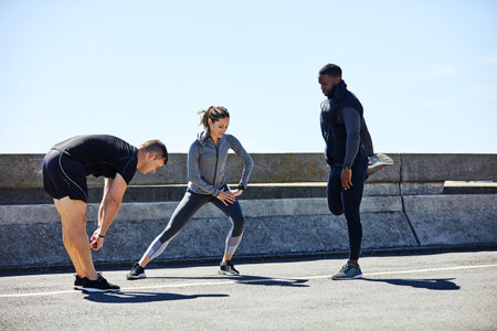 Runner, club and group stretching in city for fitness, workout and training together for marathon. Team, people or friends with warm up, exercise preparation or race with sports and activity outdoor