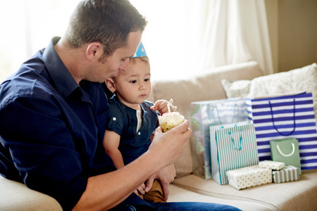 Birthday, celebration or cupcake with dad and son in living room of home together for party. Candle, dessert or gifts with boy child and single parent man in apartment for development or growth