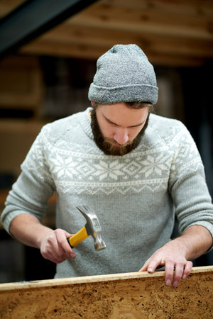 Man, carpenter and hammer with building at workshop with material, process or furniture manufacturing. Person, artisan or carpentry with wooden board, tools and equipment for production at factory