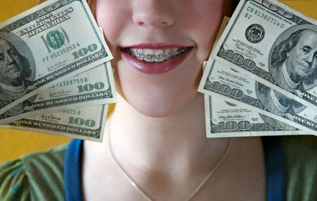 close-up image of a girl with braces holding hundred dollar billsの写真素材