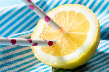 half lemon with two drinking straws painted with pink hearths on a napkin blueの写真素材
