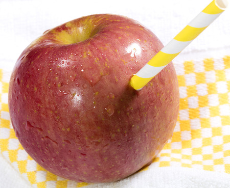 apple with drinking straw painted with yellow and white bands on a napkinの写真素材