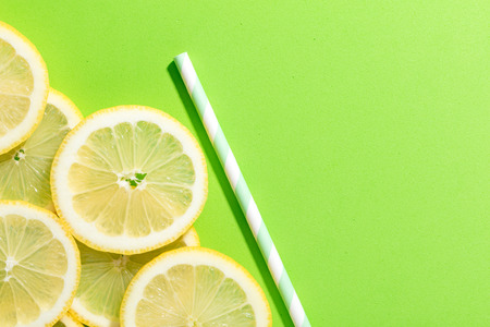 slices of lemon on green colored background with an striped strawの写真素材