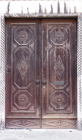 wooden brown venetian door on white stones wall, it seems old and ornamentedの写真素材