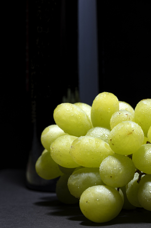 bunch of white grapes with water drops on black background with a light reflection on the bottleの写真素材