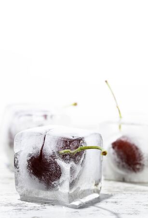 ice cubes with cherries inside on a wooden table and white backgroundの写真素材