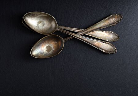 three old and worn teaspoons stacked on a slate board, free space for textの写真素材