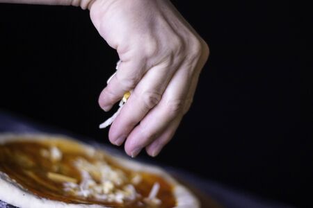 Homemade pizza dough with cheese, mushrooms, oregano, tomato, ham and flour over dark background with white and orange lights.の写真素材