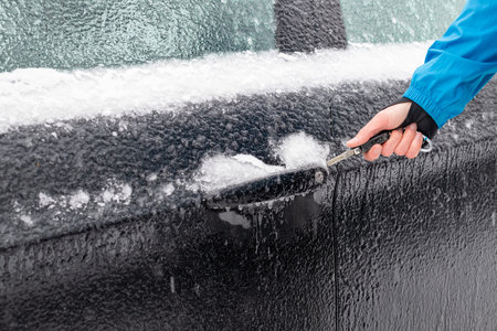 Iced car door and car lock cannot be opened. One hand holds a car key in front of the car door.