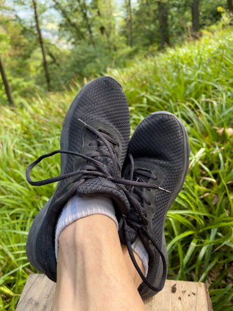 Feet in black sports shoes. A hiker rests on a bench in the forest.