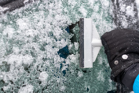 The man cleans the car from snow and ice with a scraper.