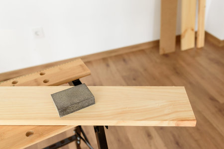 Close up shot of a wooden sandpaper on a workbench with a woman working in the background. Indoor...
