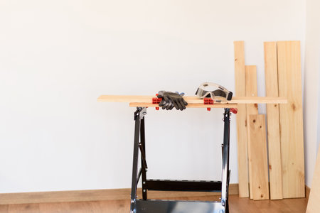 Workbench with protective glasses and safety gloves, without anyone. Inside a flat with wooden floors and white walls. It is daytime and there is natural light.の写真素材
