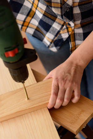 Close up of a drill drilling a screw into a piece of wood, on a wooden bench. Woman working on wooden bench. DIY enthusiast.の写真素材