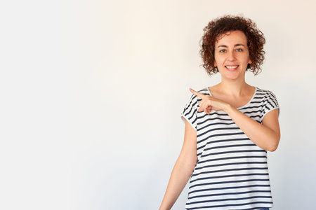 Caucasian woman with curly hair makes an approving gesture next to a shopping bag on an isolated white backgroundの写真素材