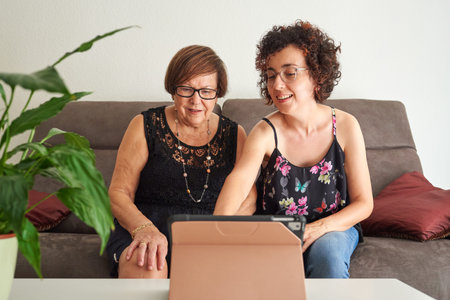 Young woman teaches elderly mother how to use digital tablet