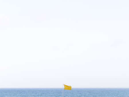 Minimalist photo of a yellow flag with the sea in the backgroundの写真素材
