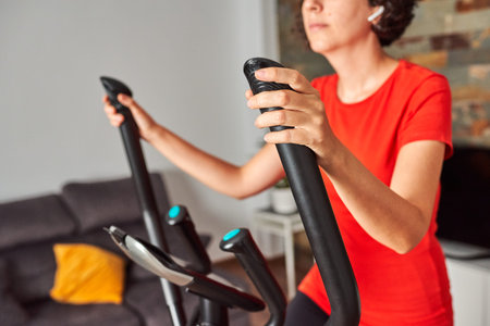 Unrecognizable woman training at home using the elliptical trainer