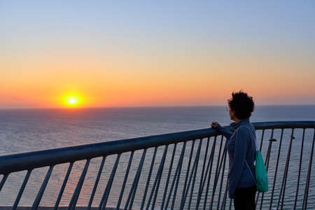 Unrecognizable woman from behind looking at sunrise over the seaの写真素材