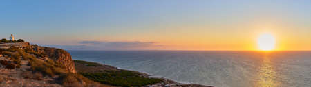 Sunrise over the sea with a small lighthouse on the coastlineの写真素材