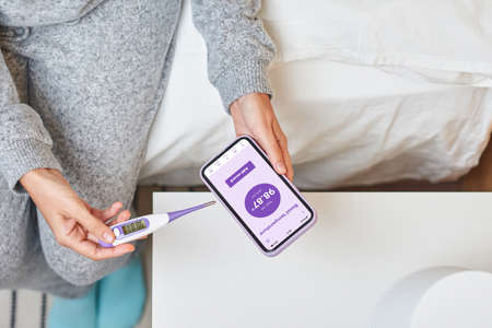 A woman records her basal temperature through her smart phoneの写真素材