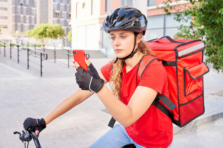A cyclist delivery girl checks the address of her next shipment with her mobile phoneの写真素材