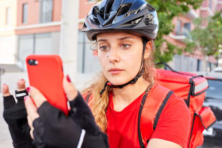 A cyclist delivery girl checks the address of her next shipment with her mobile phoneの写真素材