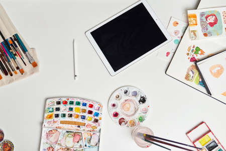 Desk of an illustrator with digital tablet watercolors and drawingsの写真素材