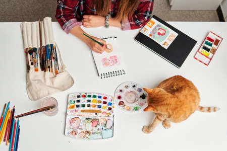 Unrecognizable woman painting in her studio with her cat on the deskの写真素材