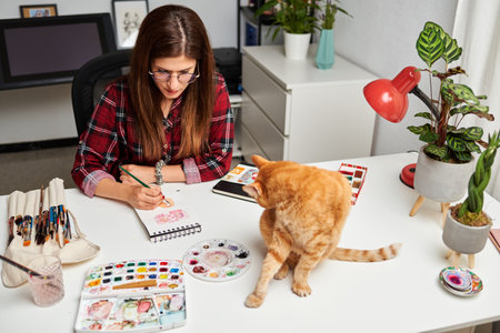 Illustrator painting in her studio with her cat on the deskの写真素材