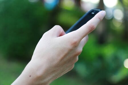 Hand holding smart mobile phone on wooden table and light blurred backgroundの写真素材