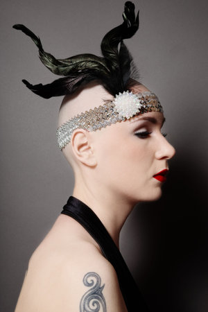 Profile of skinhead woman in black dress and stylish plumage 