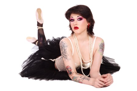 Beautiful slim young tattooed woman in ballet skirt and vintage corset lying on white backgroundの写真素材