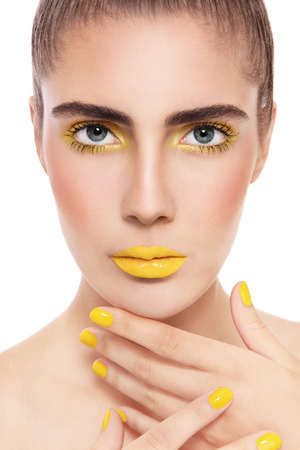 Close-up portrait of young beautiful woman with fancy yellow make-up and manicure over white backgroundの写真素材