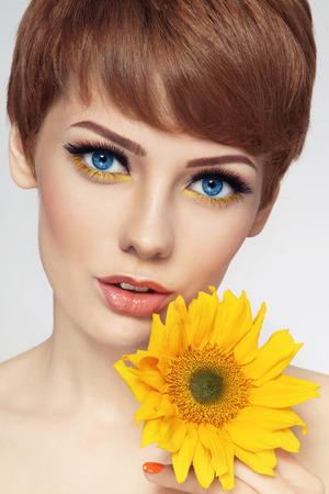 Close-up portrait of young beautiful woman with stylish make-up and sunflower in her handの写真素材