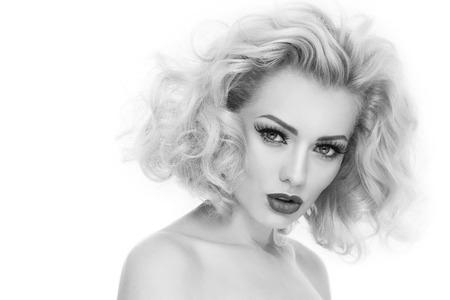 Black and white portrait of young beautiful woman with blond curly hair and false eyelashes over white backgroundの写真素材