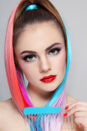 Portrait of young beautiful tanned girl with colorful ponytail and comb in her handの写真素材