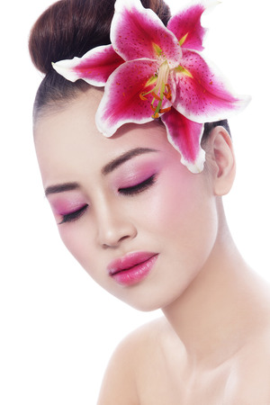 Portrait of young beautiful healthy asian girl with radiant skin and pink lily in her hair over white backgroundの写真素材