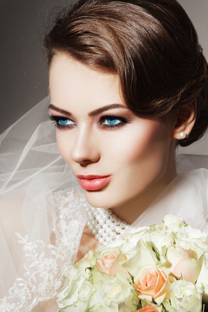 Portrait of young beautiful woman with bridal veil and bouquet of rosesの写真素材