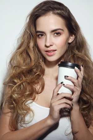 Young beautiful girl with long curly hair and cup of coffee in her handsの写真素材