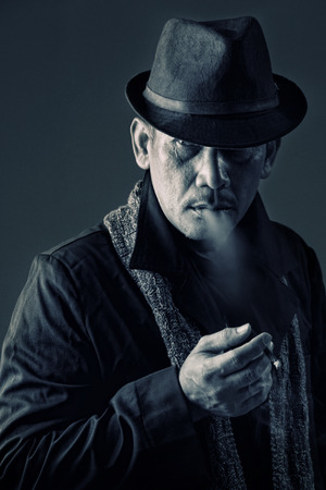 Vintage style portrait of an old private investigator smoking a cigarette in cool attitudeの写真素材