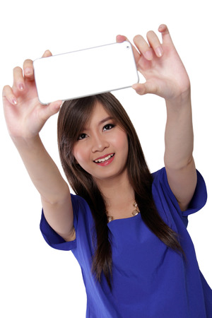 Cute Asian teenage girl taking a self picture with her smart phone camera, isolated on white backgroundの写真素材