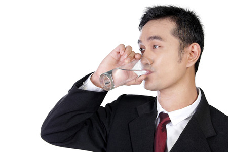 Close up portrait of young Asian businessman drinking a glass of water isolated on white backgroundの写真素材