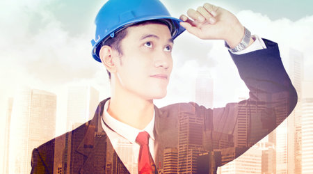 Creative imagery of modern city development. Double exposure of young architect looking up to the...