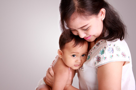 Sweet innocent baby resting on her mother's chest, over soft grey backgroundの写真素材