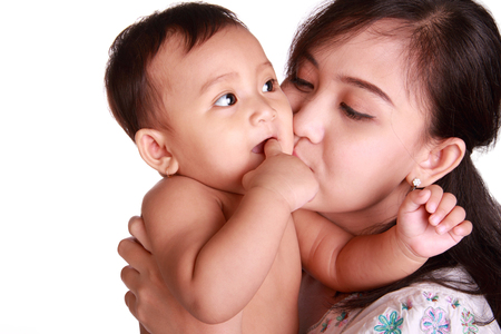 Adorable baby chewing her finger and kissed by her mom, isolated on white backgroundの写真素材